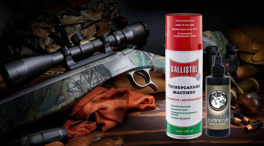 засоби для чистки зброї ballistol та boretech стоять на столі біля гвинтівки з оптикою на фоні інших комплектуючих для зброї