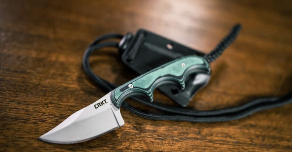 ніж на шию від бренду crkt з зеленою рукояткою лежить на столі поруч з чохлом